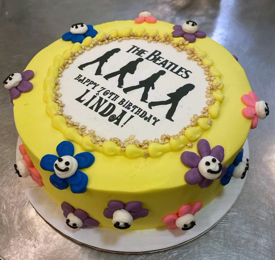 Yellow cake with The Beatles theme and floral decorations on a metallic surface.