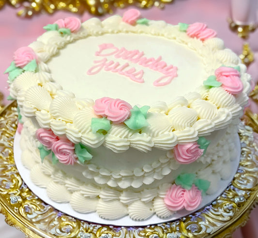 A beautifully decorated cake with white icing and pink rosettes, served on a golden platter with a Birthday message on top.