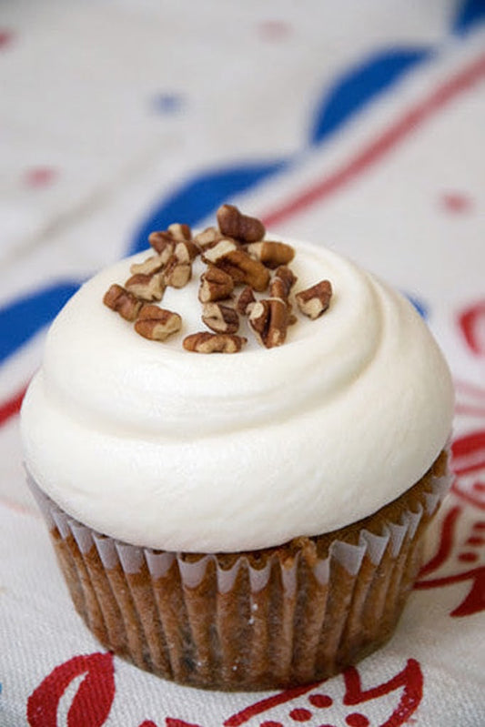 Cupcake with cream cheese frosting and chopped pecans on a patterned tablecloth
