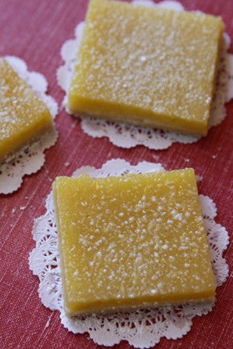 Sliced lemon bars with powdered sugar on top, placed on a red surface with lace doilies.