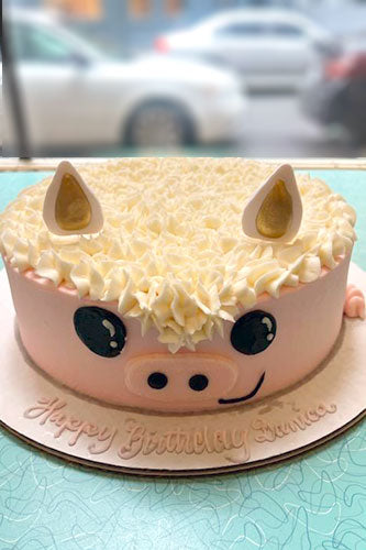 Birthday cake shaped like a pig with decorative ears on a table.