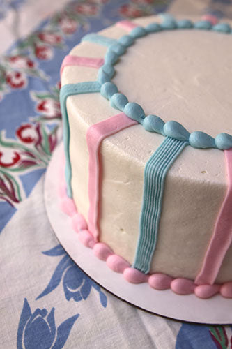 A decorated cake with alternating stripes of pastel blue and pastel pink buttercream frosting. 