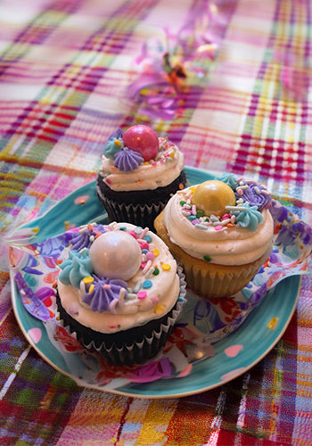 Decorative cupcakes with colorful frosting and sprinkles on a plaid tablecloth.