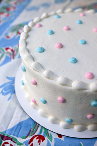A decorated cake with white buttercream icing and pastel blue and pastel pink polka dots on top and sides. 