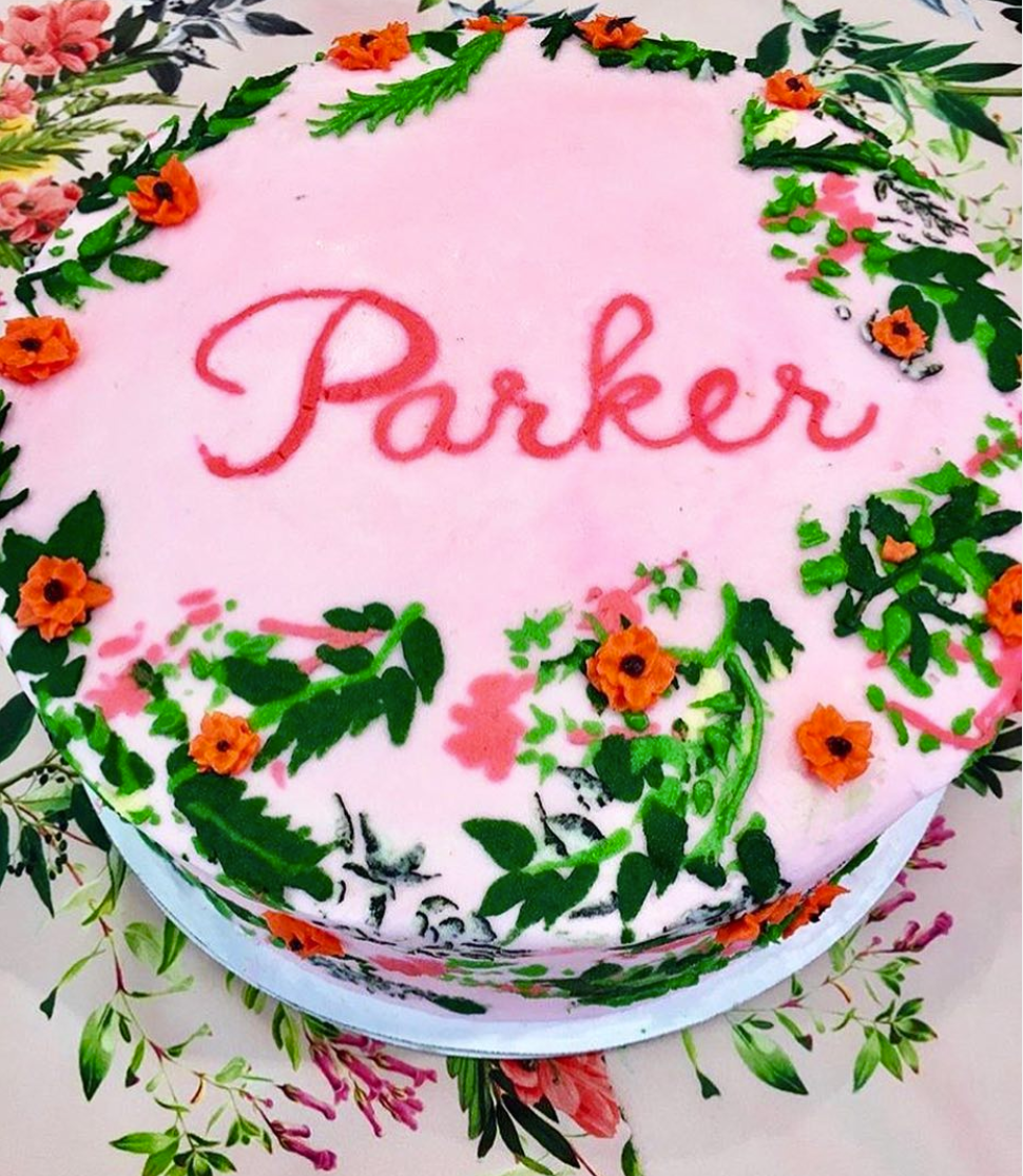 Cake with pink frosting and floral decorations with 'Parker' written on it.