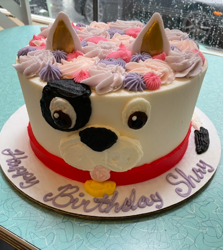 Birthday cake shaped like a dog with colorful decorations on a table.